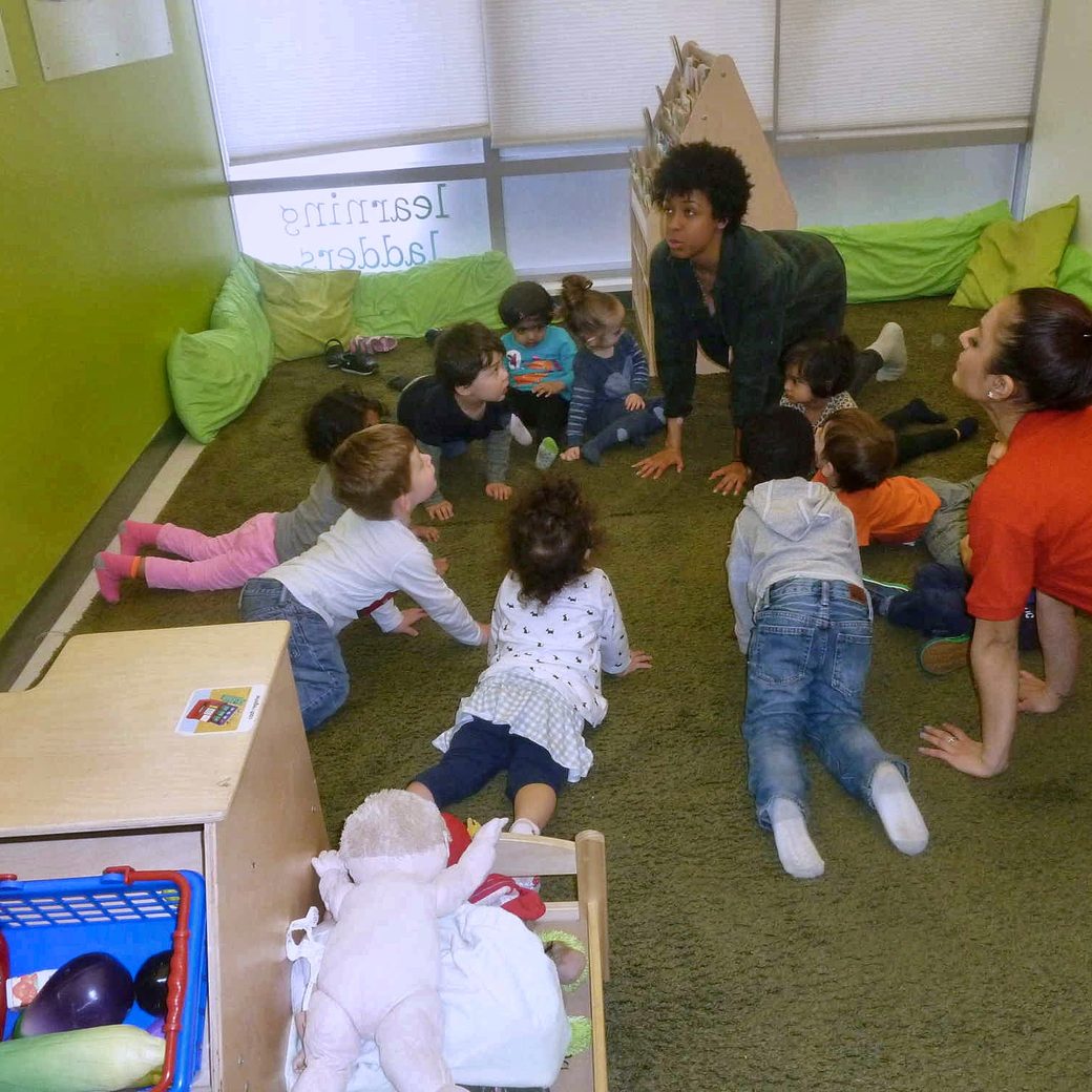 A teacher leading a circle-time activity with children on the floor