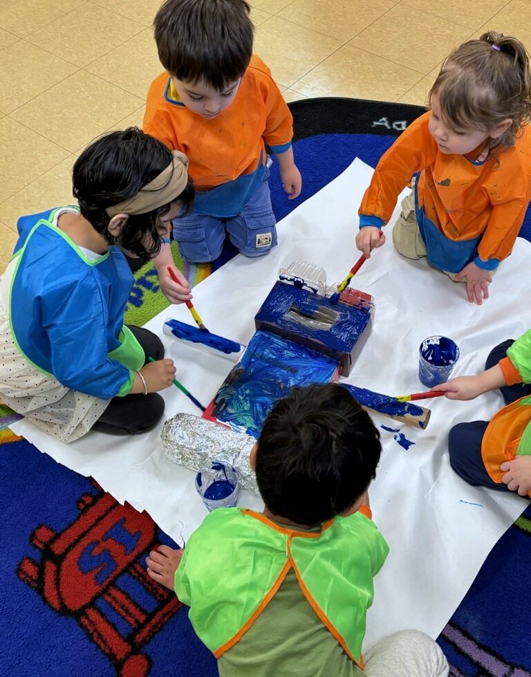 Children painting a large cardboard box together