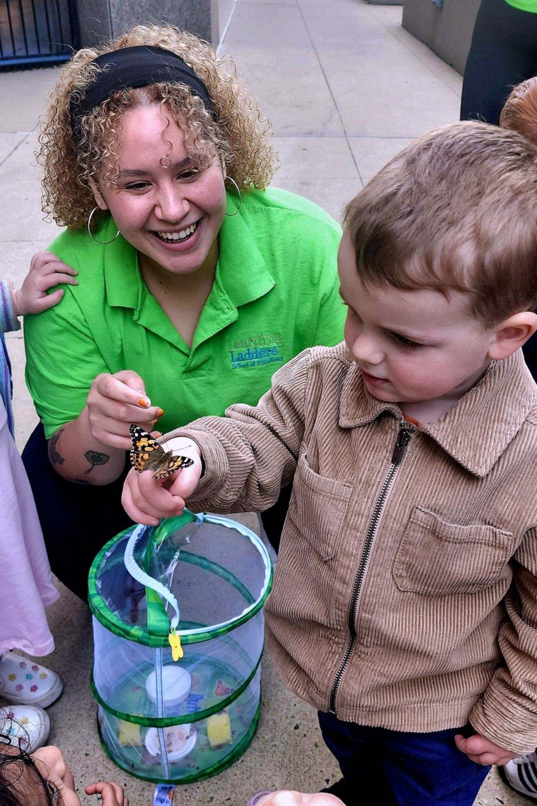 A Learning Ladders teacher laughing with a young boy over a butterfly habitat