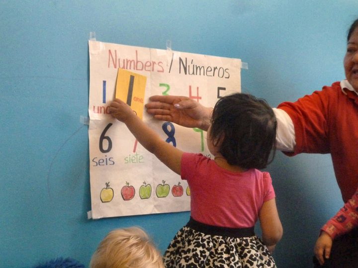 A child and teacher at a bilingual numbers chart during Spanish enrichment