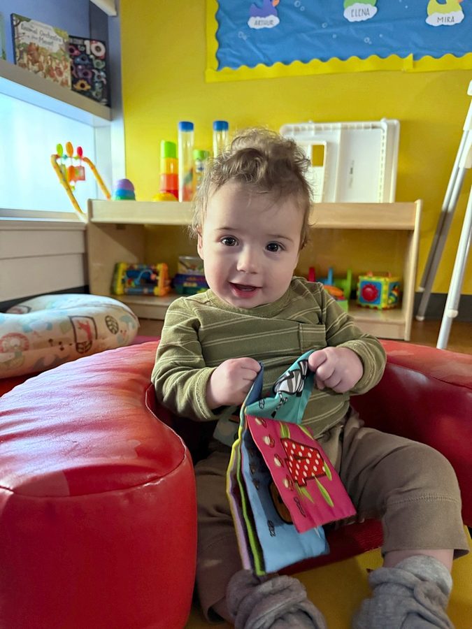 An infant exploring a cloth book on a soft seat in the Goldenberry room
