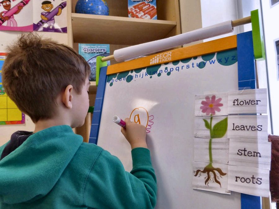 A child writing at a classroom learning chart