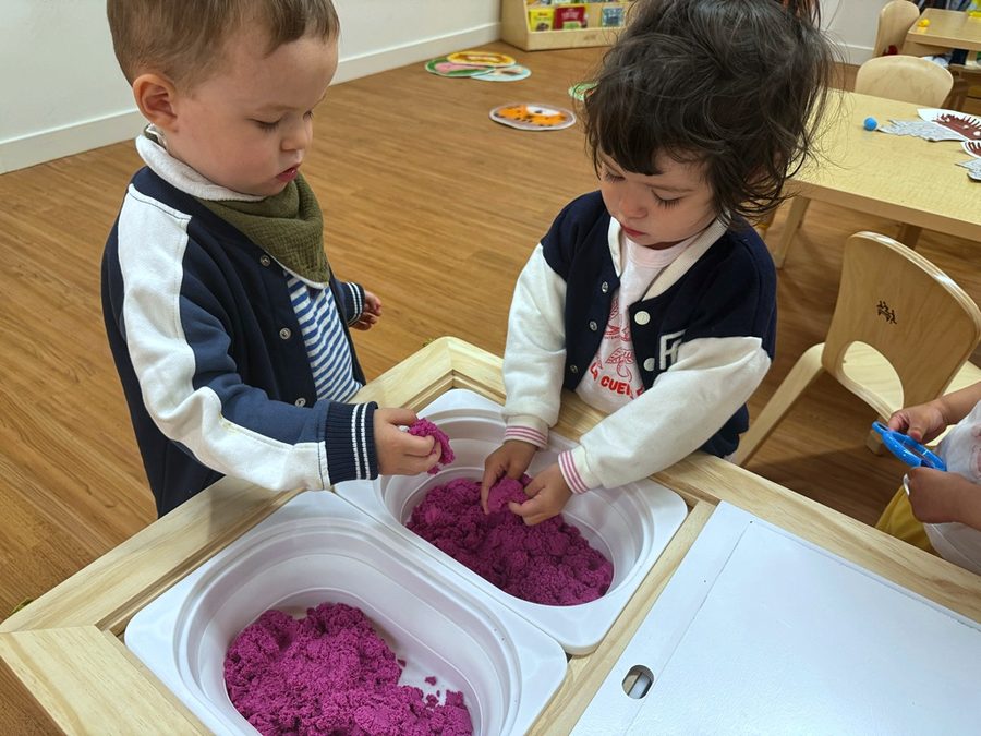 Toddlers playing at a kinetic sand table in the Strawberry room